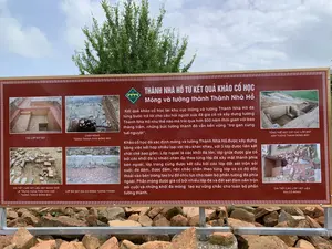 Đây là một bảng thông tin lớn đặt ngoài trời tại một địa điểm khảo cổ, có thể là khu di tích Thành Nhà Hồ. Bảng thông tin có nền màu nâu đỏ, chữ trắng, giải thích về kết quả khảo cổ học liên quan đến móng và tường thành. Phía sau bảng là cây xanh và bầu trời. Bên dưới bảng là một đống đá và gạch vỡ, có thể là hiện vật từ khu di tích.。Nội dung văn bản trên bảng như sau:。Tiêu đề chính: THÀNH NHÀ HỒ TỪ KẾT QUẢ KHẢO CỔ HỌC - Móng và tường thành Thành Nhà Hồ。Đoạn văn chính:。"Kết quả khảo cổ học tại khu vực móng và tường Thành Nhà Hồ đã từng bước trả lời cho câu hỏi người xưa đã gia cố và xây dựng tường Thành Nhà Hồ như thế nào mà trải qua hơn 600 năm thời gian với bao thăng trầm, những bức tường thành đó vẫn bền vững "trơ gan cùng tuế nguyệt".。Khảo cổ học đã xác định móng và tường Thành Nhà Hồ được xây dựng bằng việc kết hợp nhiều loại vật liệu khác nhau, với 3 lớp được liên kết chặt chẽ bao gồm: Lớp ngoài là các khối đá lớn, lớp giữa được gia cố bởi các khối đá tự nhiên chèn ốp theo từng lớp đá xây mặt thành phía bên ngoài, lớp trong cùng được kết cấu bởi các lớp đất sét trộn sỏi cuội, đá dăm, được đầm, nện chắc chắn theo từng lớp và có độ dốc thoải vào bên trong tạo trụ đỡ chịu lực cho toàn bộ phần tường đá phía ngoài. Phần móng được gia cố bởi nhiều lớp đá và đất sét đầm nền trộn sỏi cuội và những khối đá móng tạo sự vững chắc cho toàn bộ phần tường thành."。Chú thích cho các hình ảnh:。- CÁC LỚP ĐẤT SÉT。- CHÂN MÓNG TƯỜNG THÀNH PHÍA ĐÔNG BẮC。- TỔNG THỂ MẶT CẮT CÁC LỚP ĐẤT ĐẮP TƯỜNG THÀNH ĐÔNG BẮC。- CHI TIẾT CÁC LỚP VẬT LIỆU GIA CỐ MÓNG。- LỚP ĐÁ SÁT GIA CỐ MÓNG TƯỜNG THÀNH。- CHI TIẾT CỤM VẬT LIỆU XÂY DỰNG THỜI LÊ TRUNG HƯNG TRÊN KHU VỰC TƯỜNG THÀNH ĐÔNG BẮC。（日本語訳）。これは、考古学的な場所、おそらく胡朝の城跡に屋外に設置された大きな案内板です。案内板は赤褐色の背景に白い文字で、基礎と城壁に関する考古学的調査の結果を説明しています。板の後ろには緑の木々と空が見えます。板の下には石や割れたレンガの山があり、おそらく遺跡からの出土品でしょう。板に書かれている文章の内容は以下の通りです。メインタイトル：考古学的調査結果から見た胡朝の城 - 胡朝の城の基礎と城壁。メインパラグラフ：。「胡朝の城の基礎と城壁区域における考古学的調査の結果は、昔の人々がどのように胡朝の城壁を補強し建設した結果、600年以上の時と多くの浮き沈みを経てもなお、その城壁が『風雪に耐え』堅固にあり続けているのか、という問いに一歩ずつ答えを示してきました。考古学調査により、胡朝の城の基礎と城壁は、異なる種類の材料を組み合わせて建設され、密接に結合した3つの層で構成されていることが確認されました。その内容は以下の通りです。外層は大きな石のブロック、中間層は、外側の城壁表面を構築する石の層ごとに自然石のブロックをはめ込んで補強され、最内層は、砂利、砕石を混ぜた粘土の層で構成され、層ごとにしっかりと突き固められ、内側に向かって緩やかな傾斜を持ち、外側の石壁全体を支える支柱となっています。基礎部分は、何層もの石と、砂利を混ぜて突き固めた粘土、そして基礎石によって補強され、城壁全体の堅固さを生み出しています。」。写真のキャプション：。- 粘土の層。- 北東側城壁の基礎の基部。- 北東側城壁の盛土層の全体断面図。- 基礎補強材の各層の詳細。- 城壁の基礎を補強する敷石層。- 北東側城壁区域における後黎朝中興期時代の建築材料群の詳細