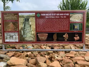 Bức ảnh chụp một tấm biển thông tin lớn màu nâu đỏ được đặt ngoài trời tại một khu di tích khảo cổ, có thể là Thành Nhà Hồ. Phía trước biển là một đống đá và gạch vỡ cổ. Phía sau là cây xanh và bầu trời. Trên biển có ghi các thông tin và hình ảnh về kết quả khảo cổ học.。Nội dung văn bản trên biển như sau:。Tiêu đề chính: "THÀNH NHÀ HỒ TỪ KẾT QUẢ KHẢO CỔ HỌC - Đàn tế Nam Giao - Tây Đô"。Đoạn văn bản: "Đàn tế Nam Giao Tây Đô là một kiến trúc quan trọng trong tổng thể khu di sản Thành Nhà Hồ. Khai quật, khảo cổ học đã xác định được cơ bản diện mạo của một đàn tế cổ với nền móng kiến trúc còn tồn tại gần như nguyên vẹn. Các vòng tường đàn và các cấp nền đàn được phát lộ và nằm gọn trong vòng tay ngai của dãy Đốn Sơn - nơi tọa lạc của đàn tế. Hàng loạt kiến trúc quan trọng và độc đáo riêng có cũng đã được xuất lộ qua khai quật, khảo cổ học như: Giếng Vua, đường Thần Đạo, Viên Đàn, hệ thống nền móng các cấp nền đàn, hệ thống cống thoát nước... cùng nhiều hiện vật độc đáo và giá trị như: Đầu chim phượng mỏ vẹt, Thống đất nung cỡ lớn, gạch ngói trang trí... Những kết quả từ khảo cổ học này đã cung cấp cho chúng ta biết được diện mạo rõ nét của một đàn tế Nam Giao thời cổ xưa trong tiến trình ra đời, tồn tại và phát triển của loại hình kiến trúc độc đáo này."。Các hình ảnh và chú thích đi kèm:。- "DẤU TÍCH ĐƯỜNG THẦN ĐẠO": Hình ảnh một con đường được khai quật.。- "SÂN NỀN LÁT GẠCH VUÔNG Ở ĐÀN TẾ NAM GIAO": Hình ảnh nền sân lát gạch.。- "TƯỜNG ĐÁ ĐÀN NAM GIAO": Hình ảnh một bức tường bằng đá.。- "CỐNG THOÁT NƯỚC NAM GIAO": Hình ảnh một lối đi hoặc cống thoát nước bằng đá.。- "CÁC LỚP MÓNG TƯỜNG ĐÀN NAM GIAO": Hình ảnh tổng thể khu vực khai quật cho thấy các lớp nền móng.。- "GIẾNG VUA": Hình ảnh một cái giếng hình vuông nhìn từ trên xuống.。- "THỐNG ĐẤT NUNG": Hình ảnh một chiếc thống (chum) bằng đất nung.。- "LÁ ĐỀ LỆCH": Hình ảnh một hiện vật trang trí bằng đất nung hình lá đề.。- "ĐẦU CHIM PHƯỢNG": Hình ảnh một hiện vật trang trí bằng đất nung hình đầu chim phượng.。- "NGÓI UYÊN ƯƠNG": Hình ảnh một viên ngói nóc có hình đôi chim uyên ương.。（日本語訳）。写真には、考古学遺跡（おそらく胡朝の城塞）の屋外に設置された、大きな赤褐色の案内板が写っている。案内板の前には古い石と割れたレンガの山がある。案内板には、考古学的成果に関する情報と画像が記載されている。案内板の文章内容は以下の通りです。メインタイトル：「考古学的成果から見る胡朝の城塞 - 南郊壇 - 西都」。本文：「西都南郊壇は、胡朝の城塞遺産群全体における重要な建築物です。発掘、考古学調査により、建築の基礎がほぼ完全な状態で現存する古代祭壇の姿が基本的に特定されました。祭壇の周壁と各段の基壇が発掘され、祭壇が位置するドンソン山脈の懐にすっぽりと収まっています。王の井戸、神道、円壇、各段基壇の基礎システム、排水溝システムなど、一連の重要かつ独特な建築物も発掘、考古学調査によって出土しました。また、オウムの嘴を持つ鳳凰の頭、大型の素焼きの壺、装飾レンガや瓦など、多くのユニークで価値のある遺物も発見されました。これらの考古学的成果は、このユニークな建築様式の誕生、存続、発展の過程における、古代の南郊壇の明確な姿を私たちに教えてくれました。」。付属の画像とキャプション：。- 「神道の痕跡」：発掘された道の画像。- 「南郊壇の正方形レンガ敷きの中庭」：レンガ敷きの中庭の画像。- 「南郊壇の石垣」：石垣の画像。- 「南郊の排水溝」：石造りの通路または排水溝の画像。- 「南郊壇の壁の基礎層」：基礎層を示す発掘エリア全体の画像。- 「王の井戸」：上から見た四角い井戸の画像。- 「素焼きの壺」：素焼きの壺（thống/chum）の画像。- 「非対称の菩提樹の葉」：菩提樹の葉の形をした素焼きの装飾品の画像。- 「鳳凰の頭」：鳳凰の頭の形をした素焼きの装飾品の画像。- 「鴛鴦瓦」：おしどりのつがいをかたどった棟瓦の画像。