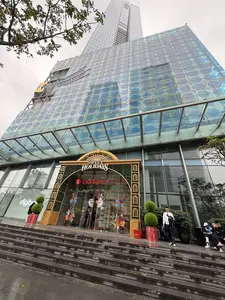 Bức ảnh chụp từ góc thấp hướng lên lối vào của một tòa nhà chọc trời hiện đại bằng kính. Đây là trung tâm thương mại Lotte, lối vào được trang trí lộng lẫy cho dịp lễ hội với một cổng chào lớn màu vàng và xanh lá. Xung quanh lối vào được trang trí theo chủ đề Giáng sinh với các hình ngựa gỗ và người lính chì. Một vài người đang đứng và ngồi trên các bậc thang rộng phía trước. Phía trên là tòa tháp cao vút bằng kính và bầu trời có vẻ u ám.。（日本語訳）。ガラス張りの近代的な高層ビルの入り口を、ローアングルから見上げて撮影した写真。これはロッテのショッピングセンターで、入り口は祝祭シーズンに合わせて黄色と緑色の大きなアーチで華やかに飾られている。入り口の周りは、木馬と鉛の兵隊の像でクリスマスのテーマに沿って飾られている。前面の広い階段には、何人かの人々が立ったり座ったりしている。上にはガラス張りのそびえ立つタワーがあり、空は曇っているようだ。