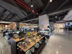 Bên trong một cửa hàng bán đồ gia dụng và dụng cụ nhà bếp cao cấp, có vẻ như nằm trong một trung tâm thương mại. Không gian rộng rãi, sáng sủa với sàn gạch bóng loáng và hệ thống đèn rọi phức tạp trên trần nhà. Ở phía trước, một quầy hàng trưng bày nhiều loại nồi và chảo inox sáng bóng của thương hiệu SCANPAN được sắp xếp trên kệ gỗ. Ở giữa, một cột trưng bày các sản phẩm của thương hiệu ZOJIRUSHI, có biển giảm giá 30%. Các khu vực khác trong cửa hàng bày bán nhiều thiết bị điện gia dụng như máy xay sinh tố, máy lọc không khí, và các dụng cụ nhà bếp khác. Có một vài khách hàng đang đi lại và xem hàng trong cửa hàng.。（日本語訳）。高級な家庭用品とキッチン用品を販売する店の内部で、ショッピングセンターの中にあるようだ。広々として明るい空間で、床は光沢のあるタイル張り、天井には複雑なスポットライトシステムがある。前方には、SCANPANブランドの光沢のあるステンレス製の鍋やフライパンが多数、木製の棚に並べられた売り場がある。中央には、ZOJIRUSHI（象印）ブランドの製品を展示する柱があり、30%割引の表示がある。店内の他のエリアでは、ミキサー、空気清浄機などの多くの家電製品や、その他のキッチン用品が販売されている。店内では数人の客が歩き回り、商品を見ている。