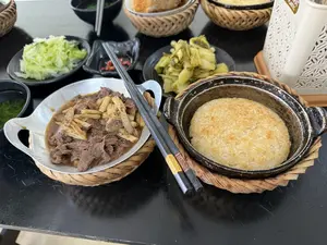 Trên bàn ăn màu đen bày một bữa ăn Việt Nam, bao gồm một niêu cơm cháy vàng giòn và một chảo thịt bò xào măng. Các món ăn kèm gồm có dưa cải muối chua, rau bắp cải luộc, một bát canh và một chén nước chấm có ớt tươi. Các món ăn được đặt trên đế lót bằng tre đan. Một đôi đũa được đặt trên chảo thịt bò.。（日本語訳）。黒い食卓の上にベトナム料理が並べられており、黄金色でカリカリのおこげが入った土鍋一つと、牛肉とタケノコの炒め物が入ったフライパン一つが含まれる。付け合わせには、高菜の漬物、茹でキャベツ、スープ一杯、そして生の唐辛子が入ったタレの小鉢一つがある。