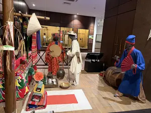 画像内には判読可能な文字は存在しません。博物館の展示室で、様々な民族衣装を着たマネキンが展示されています。赤、白、青の衣装を着たマネキンがおり、太鼓や扇子などの小道具も見えます