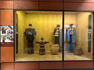 [ガラスケースの中に、民族衣装を着たマネキン数体と籠が展示されている。左の壁には複数の写真が貼られている