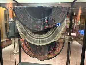 ガラスケースの中に、黒、白、そしてカラフルな装飾が施された3つの扇状のプリーツスカートが展示されている
