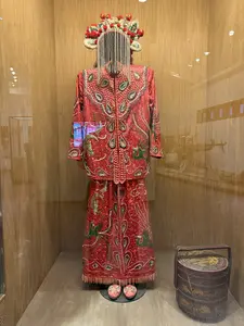 画像には文字がありません。ガラスケースの中に、赤地にビーズや刺繍で豪華に装飾された伝統衣装一式が展示されています。頭にはビーズのすだれがついた髪飾りが装着され、衣装の隣には漆塗りの重ね箱が置かれています