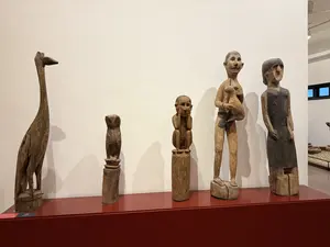 画像内には看板や説明文などの文字情報はありません。鳥や人物などをかたどった5体の木彫りの像が、赤い展示台の上に並べられています