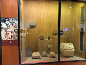博物館の展示ケース。中には竹で編まれた籠や帽子、陶器などが展示されている。左側には生活の様子を写した写真が複数枚飾られている。判読可能な看板や説明文はない