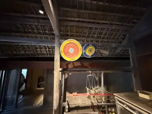 [木造家屋の梁の上に、赤と黄色、青と黄色で彩られた2つの円形の盾が飾られている