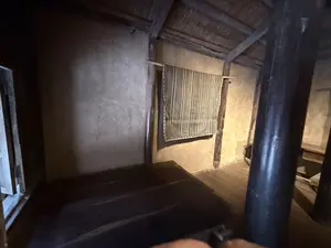 Bên trong một ngôi nhà truyền thống có tường đất và cột gỗ. Một tấm vải sọc được treo trên tường.（土壁と木の柱でできた伝統的な家屋の内部。壁には縞模様の布が掛けられている