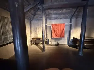 木の柱と土壁でできた家屋の内部。中央に赤い布が掛けられている]