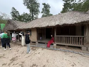 茅葺き屋根の伝統的な家屋の前に数人の人々がいる。画像内に看板や読み取れる文字はない