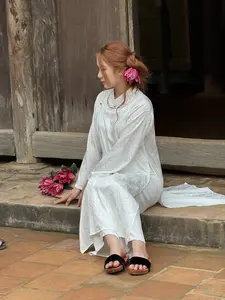 白い伝統衣装を着た女性が、古い木造家屋の石段に座っています]