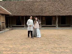 画像には文字がありません。伝統的なベトナムの木造家屋の中庭で、伝統衣装を着た男女が歩いている