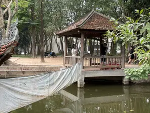 池のほとりに建てられた木造の東屋。周囲は木々に囲まれ、数人の人物がいる