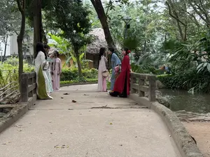 画像には、公園のような場所で小川にかかる橋の上に立つ、伝統的な衣装を着た複数の人物が写っている。看板や碑文など、読み取れる文字は一切ない