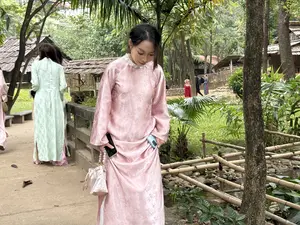 ピンク色のアオザイを着た女性が、屋外の公園のような場所の小道を歩いている。画像内に読み取れる文字はない