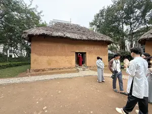 茅葺き屋根を持つ土壁の家屋が写っており、その前には数人の人物がいる]