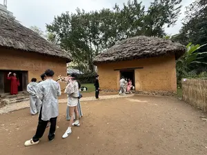 藁葺き屋根の土壁の家が2棟建っており、その周りに人々がいる]