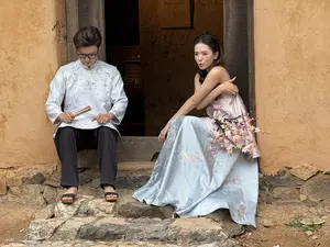 [土壁の家屋の石段に、伝統的な衣装を着た男女が座っている