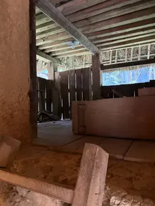 画像には看板や説明文などの文字は一切写っていません。土壁と木材で造られた伝統的な家屋の内部のようです。天井には太い梁が渡され、奥には木製の柵のようなものが見えます